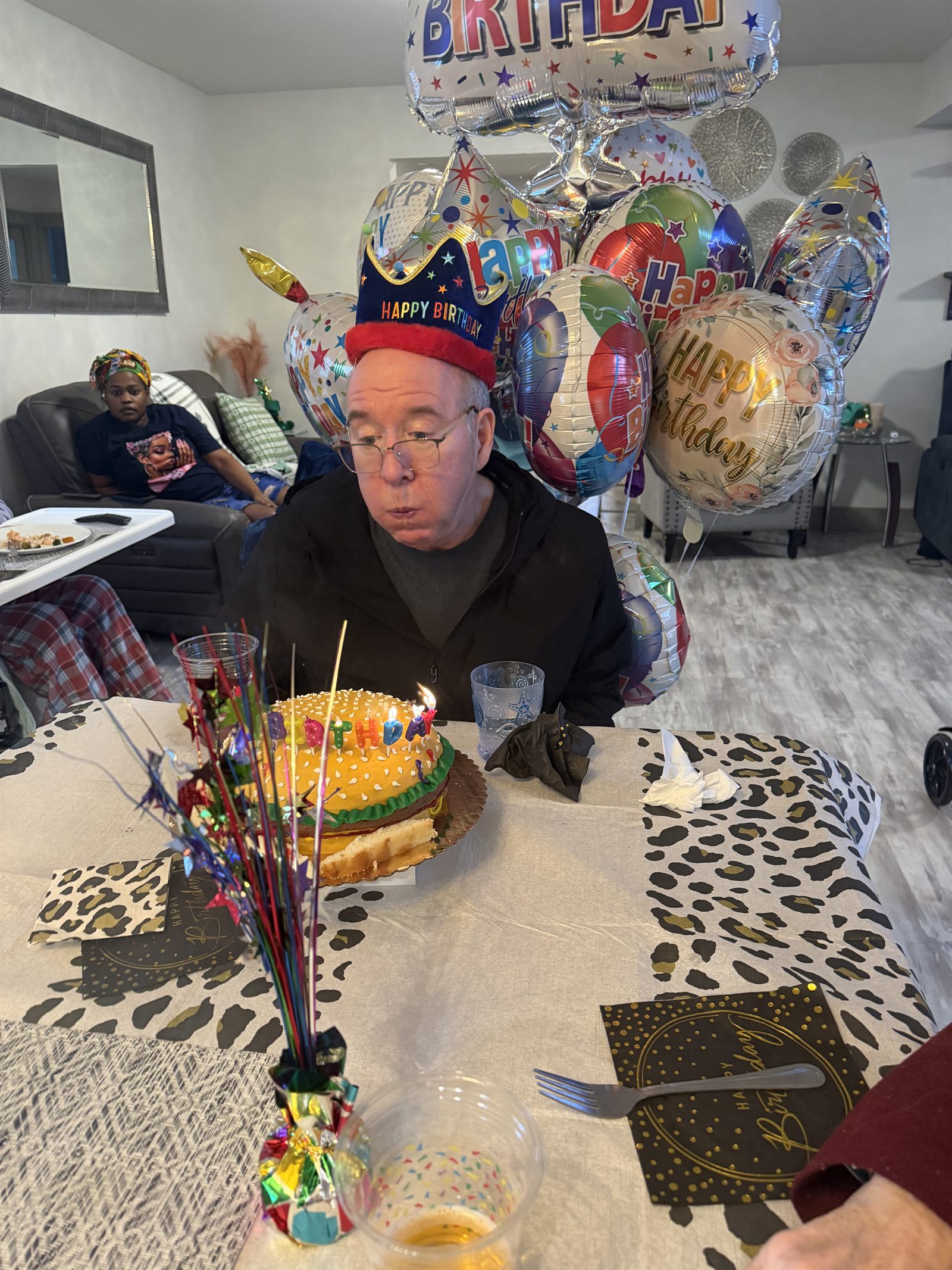 A resident in a birthday crown blowing out the candles on his cake