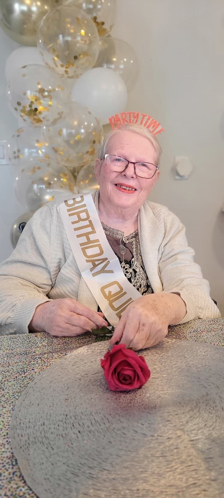 A resident wearing a birthday sash and party crown, holding a red rose